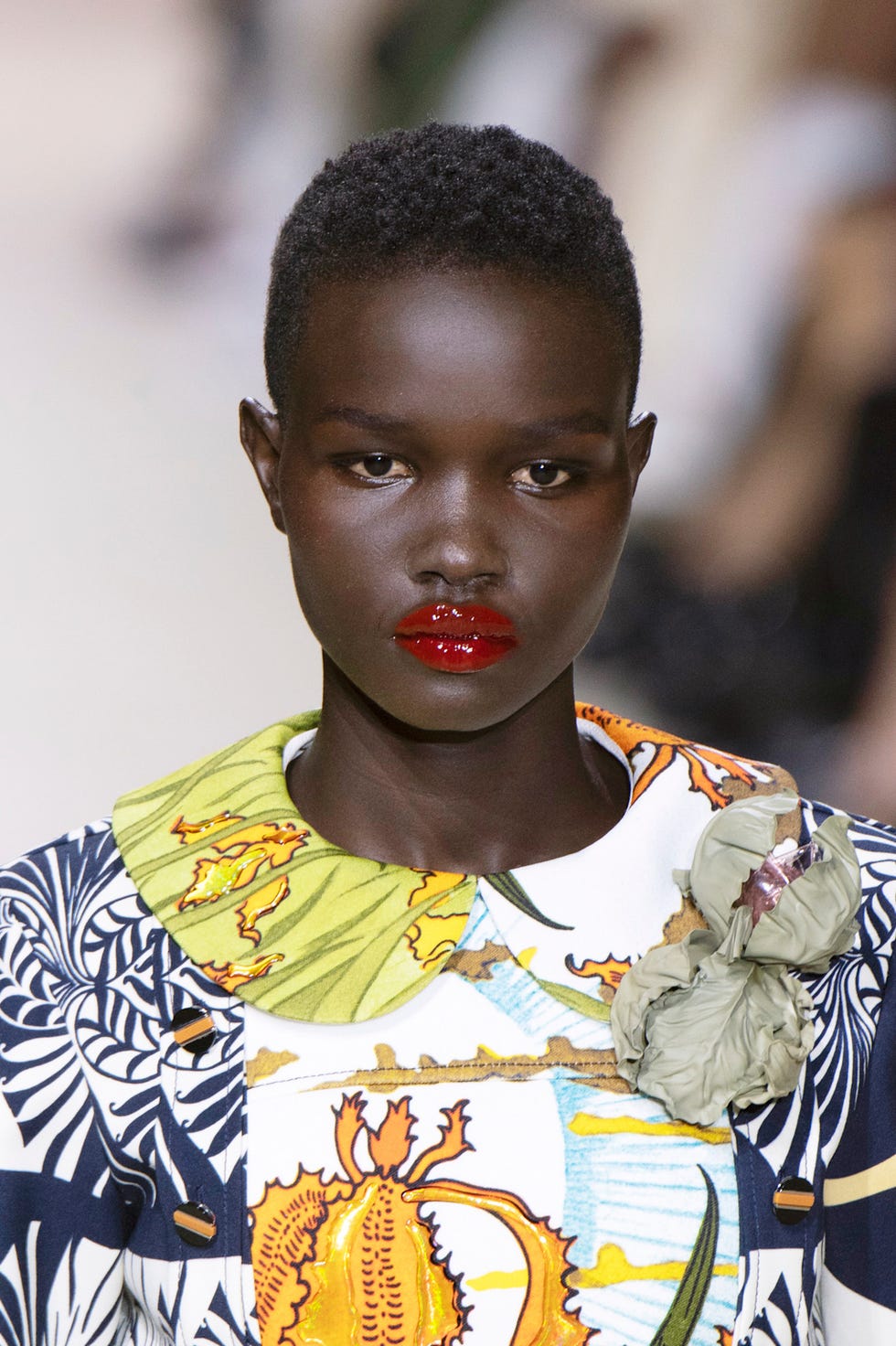 Fashion model showcasing an outfit with vibrant botanical patterns and a decorative brooch