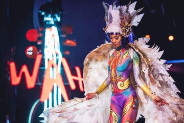 a performer in colorful body paint and elaborate costume poses on stage