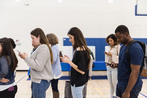 young voters waiting in line to vote, looking at their phones