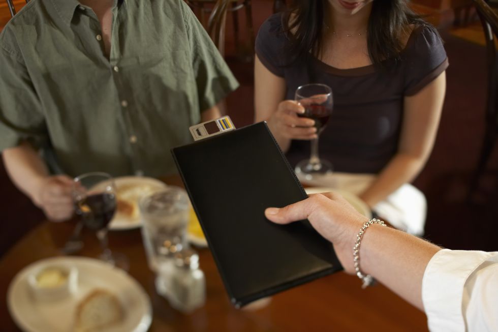 waitress handing bill to couple in restaurant