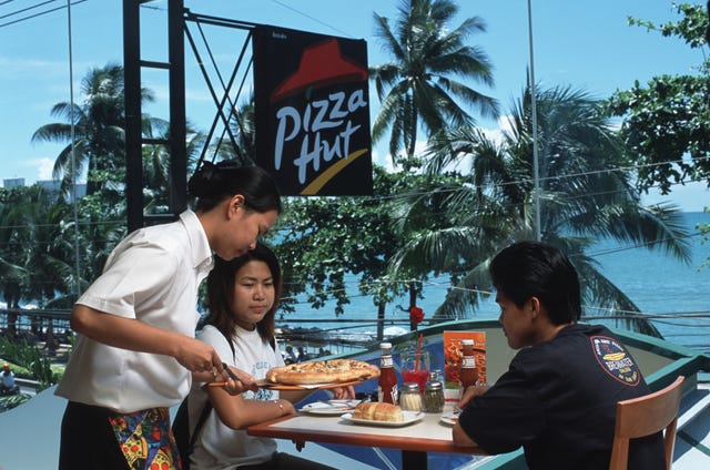 a waitress serves pizza to a thai couple inside a pizza hut