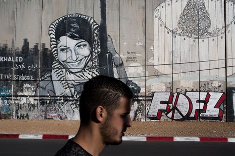 Een Palestijnse man loopt langs de muur in Bethlehem bij een graffitiafbeelding van Leila Khaled een Palestijnse activiste die bekendstaat als de eerste vrouw die een vliegtuig kaapte