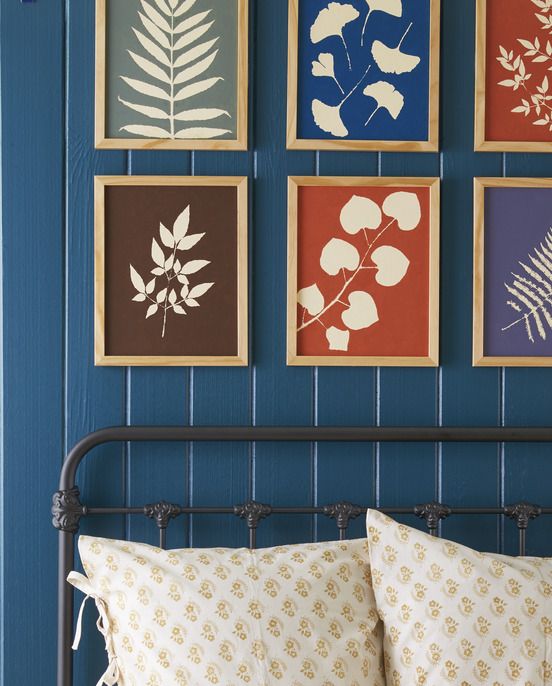 a grid of colorful botanical like prints hang above a bed in wooden frames