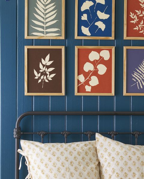 a grid of colorful botanical like prints hang above a bed in wooden frames