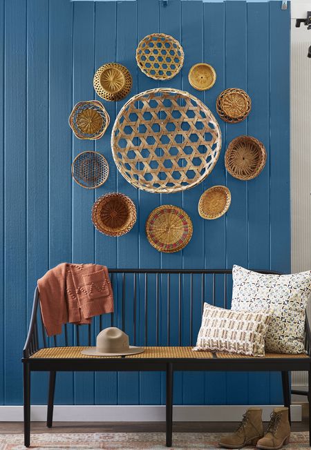 baskets of all styles arranged on a wall that is painted blue with a bench in front of it
