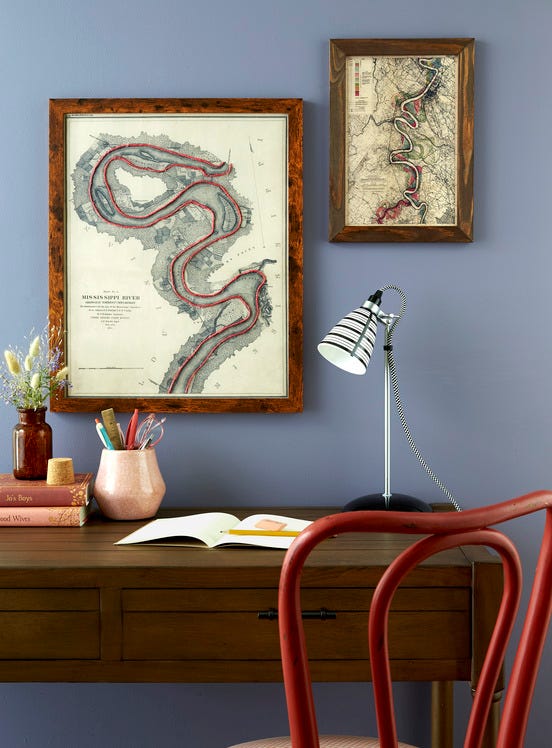 a pair of maps hang on a wall above a desk