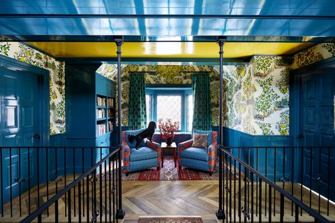 landing
with custom
wrought iron pillars,
a second floor bridge
across the carvedout
stairwell appears
suspended from the
ceiling wallpaper
josef frank from
schumacher curtains
clare louise frost
rug landry  arcari
chairs lee industries,
upholstered in carolina
irving blue and tulu
textiles red fabrics
