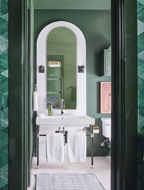 guest bathroom adjoining the main room coated in green paint with mixed brass, black, and polished nickel, and an arched backsplash and mirror behind the console sink

fixtures signature hardware
towels tencel, macy’s oake
paint farrow  ball 
lighting circa lighting 
backsplash caesarstone
rug serena  lily