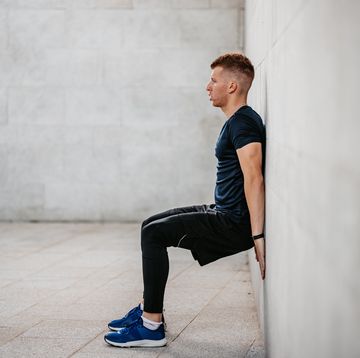 a handsome young man doing the wall sit exercise outdoors