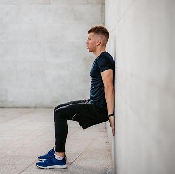 a handsome young man doing the wall sit exercise outdoors