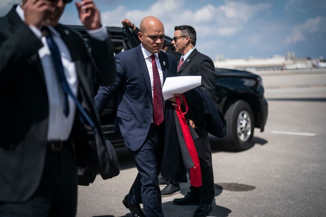 walt nauta, wearing a blue suit and red tie, walks past two men while leaving a black car on an airport tarmac