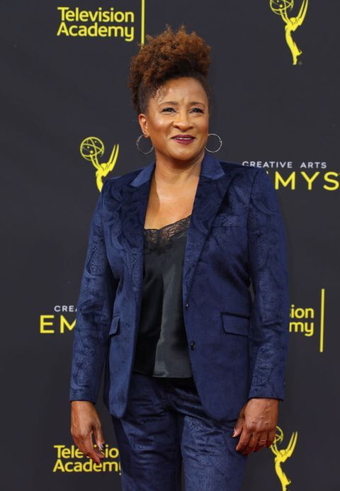 wanda sykes wears a blue patterned suit over a black lacy camisole on the red carpet her hair is short and curly and she wears hoop earrings and dark lipstick