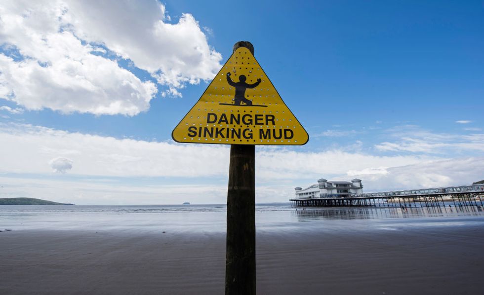 a sign on a wet sandy beach reads "danger sinking mud"
