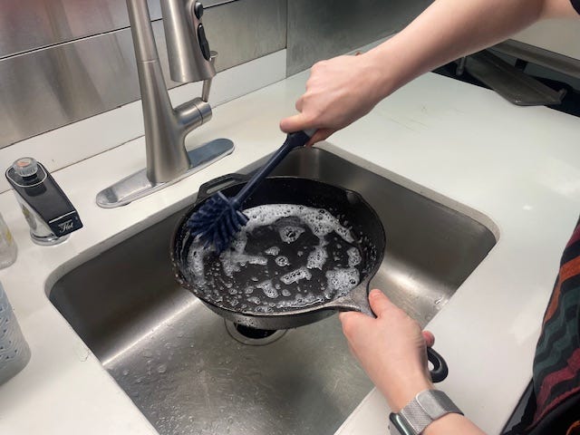 cleaning a cast iron skillet with soapy water and a brush