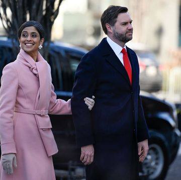 usha vance and jd vance walk outside, she smiles and looks back to the left as she holds his elbow, he smiles as he looks forward to the right