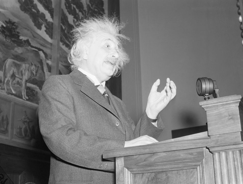 albert einstein standing at a podium and gesturing with his left hand while speaking
