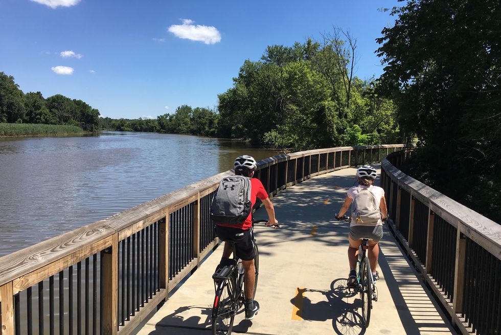 two people ride bikes on a path along a river