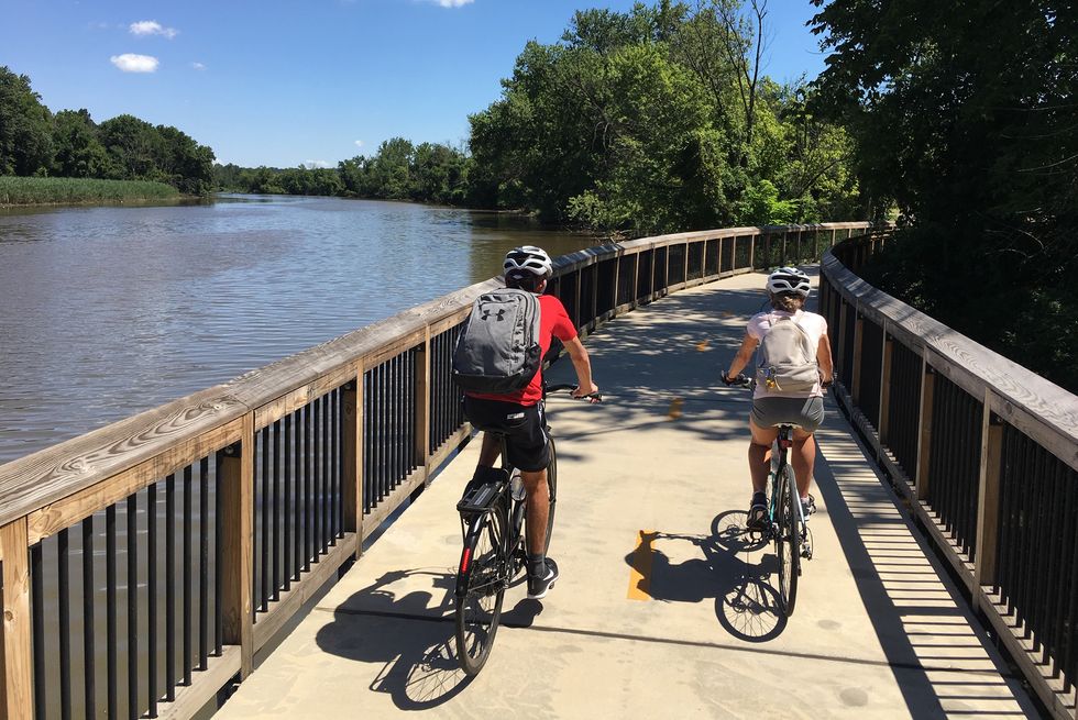 two people ride bikes on a path along a river