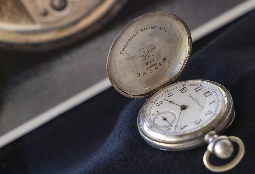 a silver pocket watch rests open on a table, it has theodore roosevelt inscribed on the inside