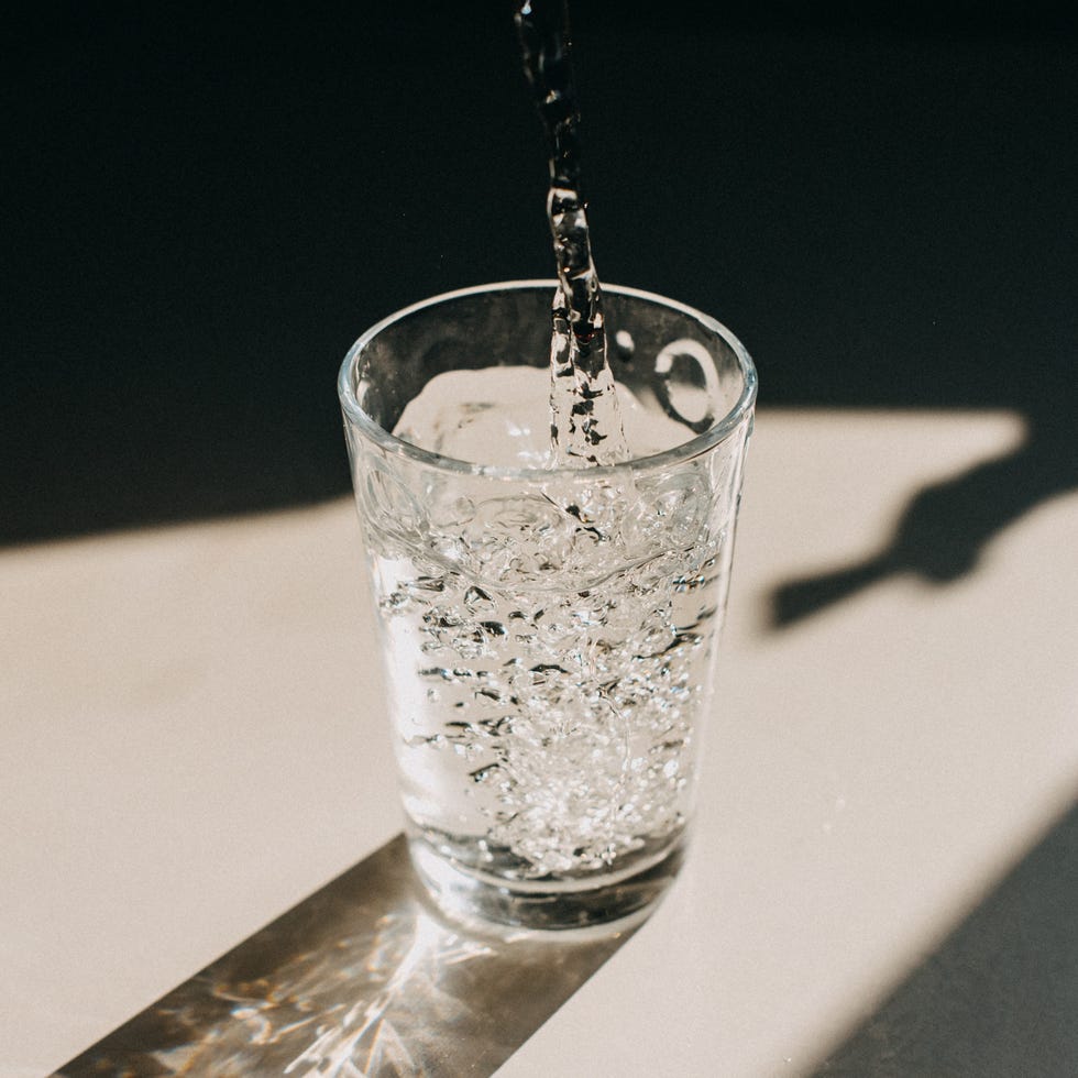 water being poured in a glass of water that cast a beautiful shadow on a white kitchen countertop copy space