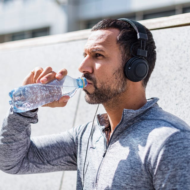 man having a break from exercising wearing headphones and drinking from bottle