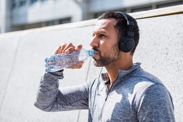 man having a break from exercising wearing headphones and drinking from bottle