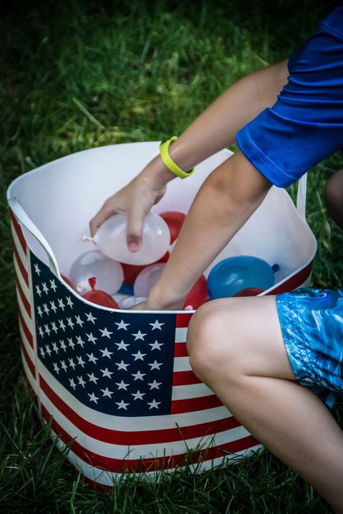 child picking small red, white and blue water balloons out of tub with american flag on it
