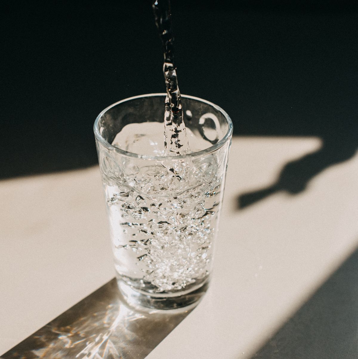 water being poured in a glass of water that cast a beautiful shadow on a white kitchen countertop