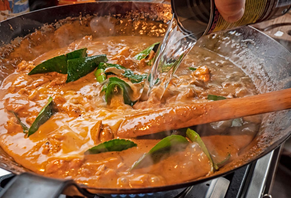 water is added to a wok to thin the creamy sauce of a thai red chicken curry