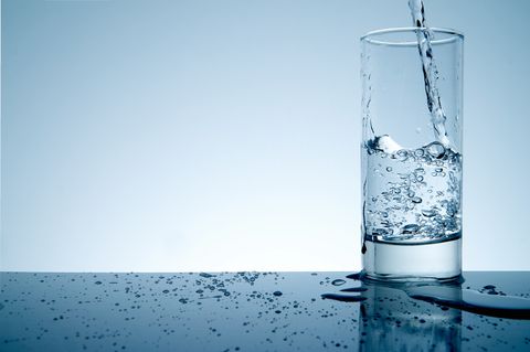 Water Pouring In Glass On Table Against White Background