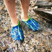 kid standing in rocky river wearing blue and green water shoes