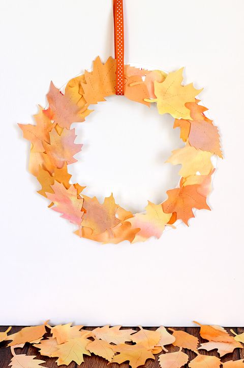 paper wreath adorned with watercolor cutouts of fall leaves, hung from orange ribbon with white polka dots