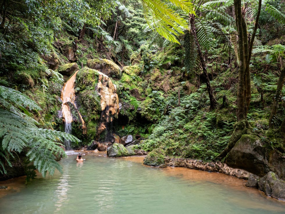 a waterfall of warm volcanic water in majestic forest environment with persons swimming island of sao miguel, azores islands, portugal europe