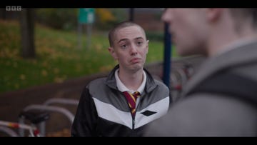 waterloo road, boz in school uniform in front of a bike rack at daytime, out of focus preston on the right side of the frame