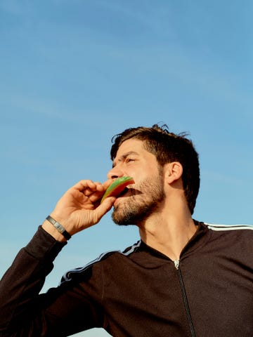 Person wearing a black athletic jacket outdoors holding an object to their mouth