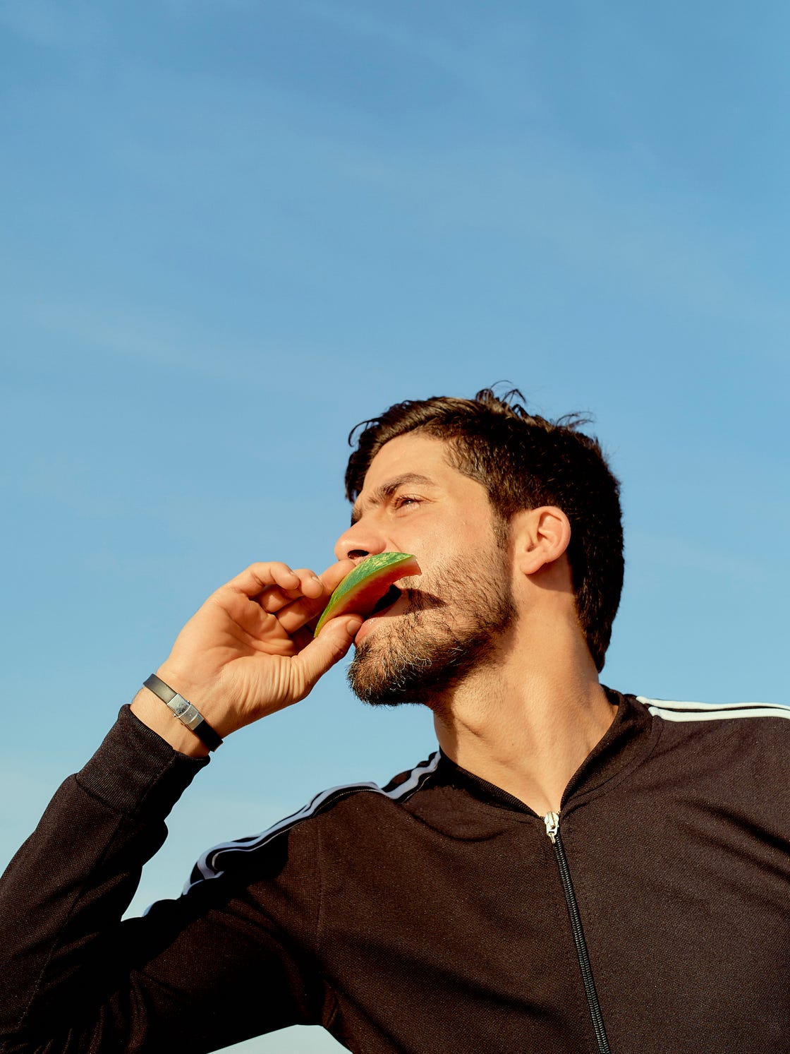 Person wearing a black athletic jacket outdoors holding an object to their mouth