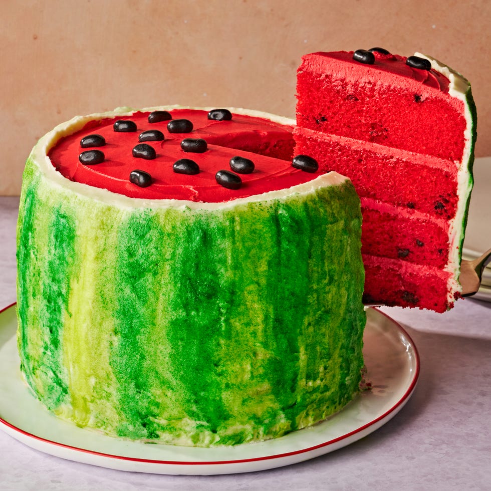 cake colored and decorated to look like a watermelon, with green stipple frosting on the outside, red frosting for the top, and black jelly beans for the seeds