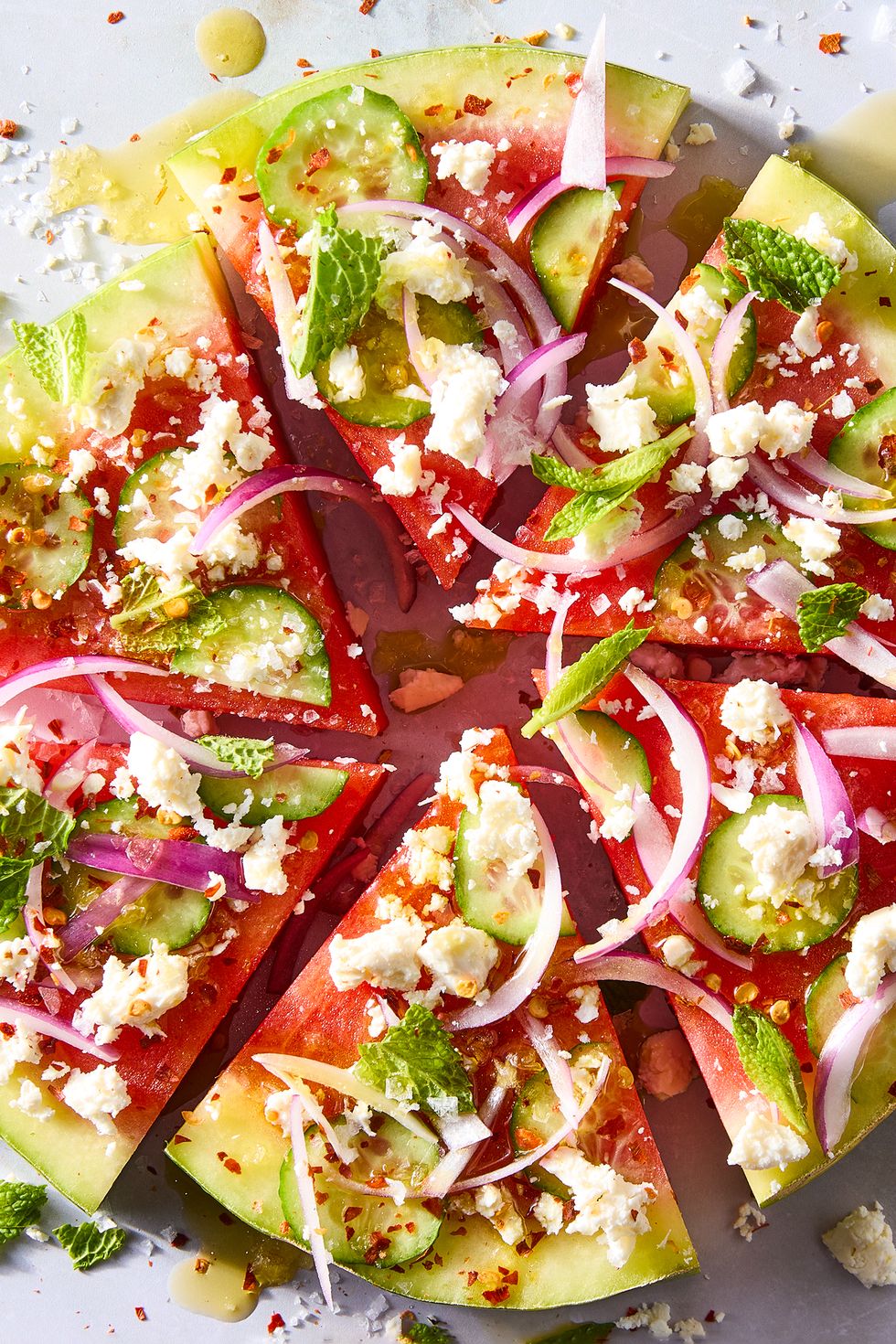 watermelon slices topped with red onion, sliced cucumbers, feta, and mint