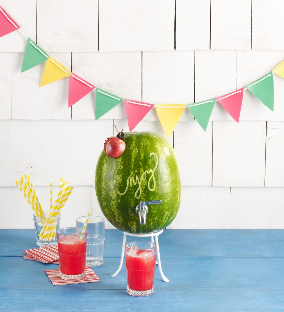 a watermelon dispensing pink cocktails into glasses