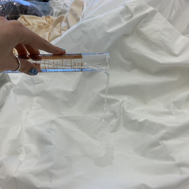 a lab analyst pouring a set amount of distilled water onto a mattress protector to evaluate its waterproof abilities