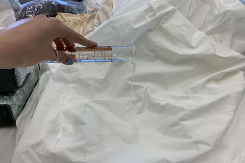 a person pouring water from a graduated cylinder onto a mattress protector to test if it is waterproof