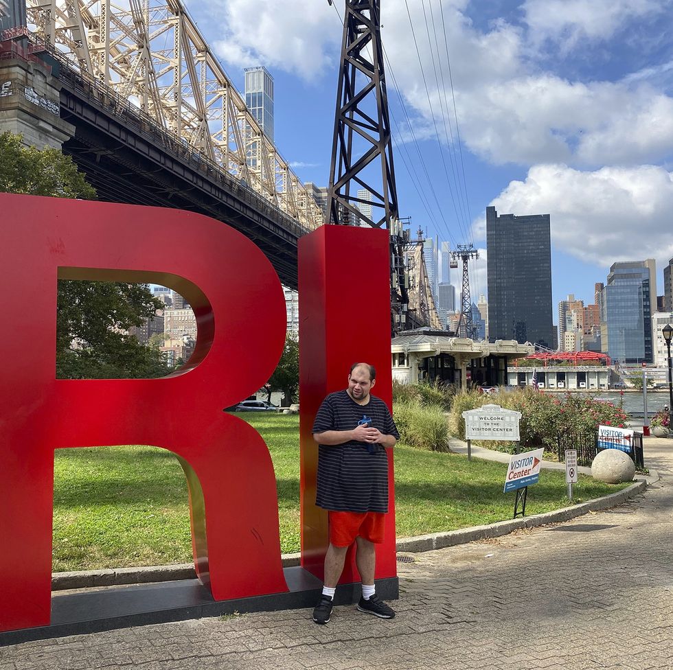 tony poses in front of a sculpture that says ri with a park and city skyline behind him