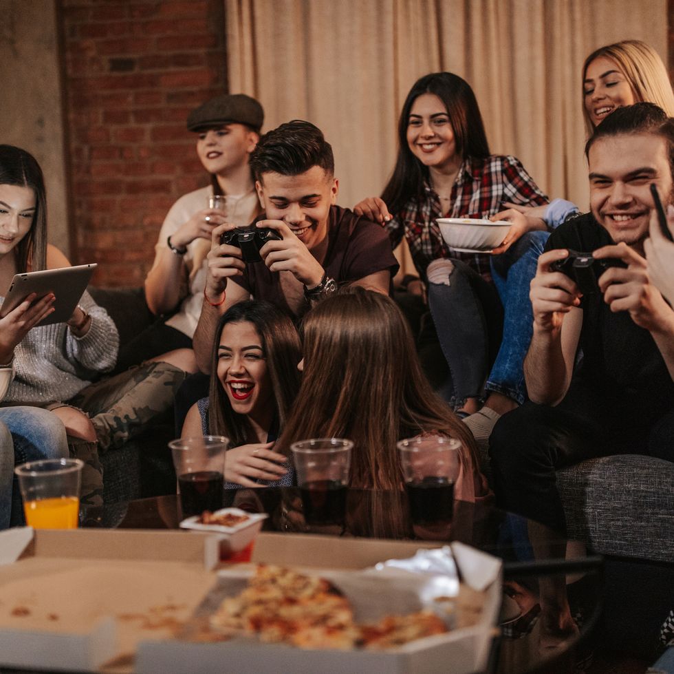 a big rowdy group of teens playing video games and eating pizza