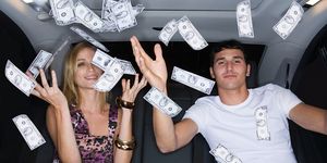 una pareja joven lanzando billetes al aire en el interior de un coche