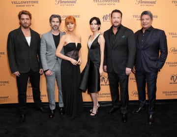 cast members of a show pose at a promotional event with a branded backdrop