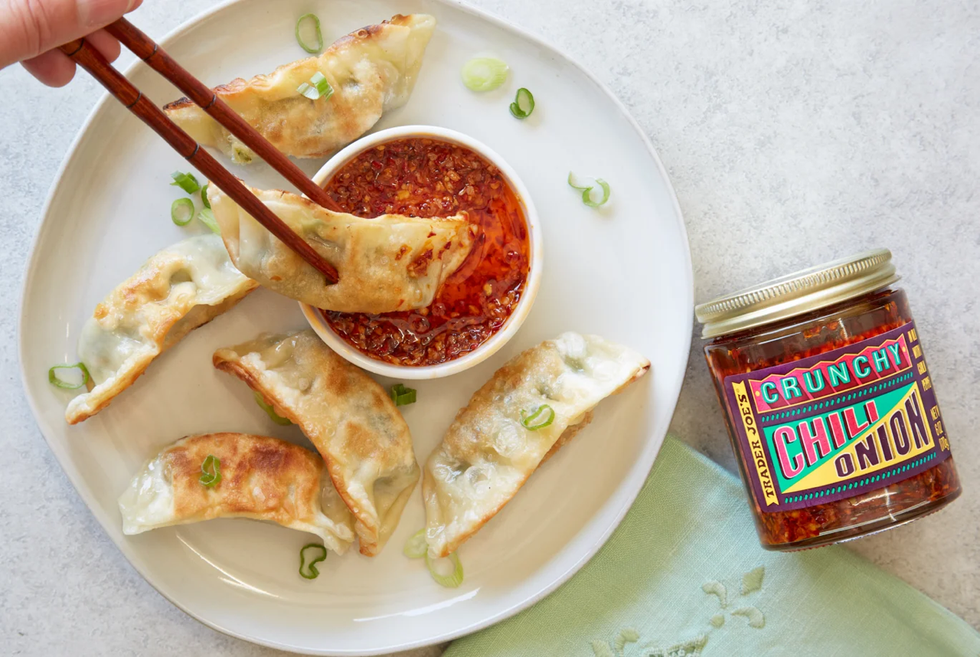 trader joe's cruncy chili onion in a small dish on a plate with gyoza, a hand with chop sticks dipping one into the sauce
