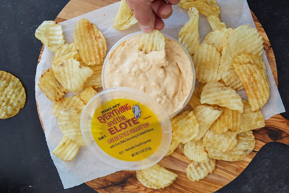 trader joe's everything and the elote greek style yogurt dip opened, with a chip being dipped, and surrounded by more chips