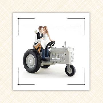 two wedding cake toppers one of a farmer and his wife on a tractor and one of the word love both placed on a cream background