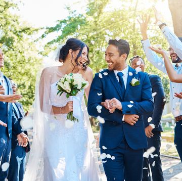 wedding guests throwing rose petals confetti tradition over bride and groom on their special day. newlywed couple walking past friends and family