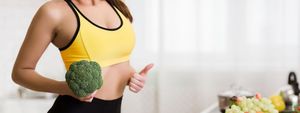 Weight loss concept. Girl holding broccoli and showing thumb up